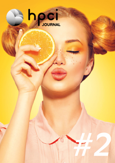 Cover HPCI Journal #2 showing a red-haired young women holding a slice of orange in front of her right eye, eyes closed, mouth like kissing. Background of the foto is yellow-orange